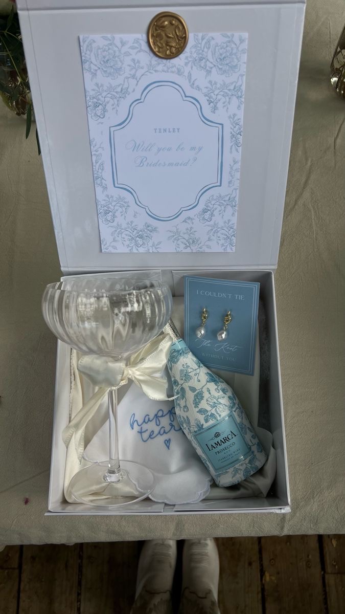 An open white proposal box with a coupe glass and a will-you-be-my-bridesmaid card